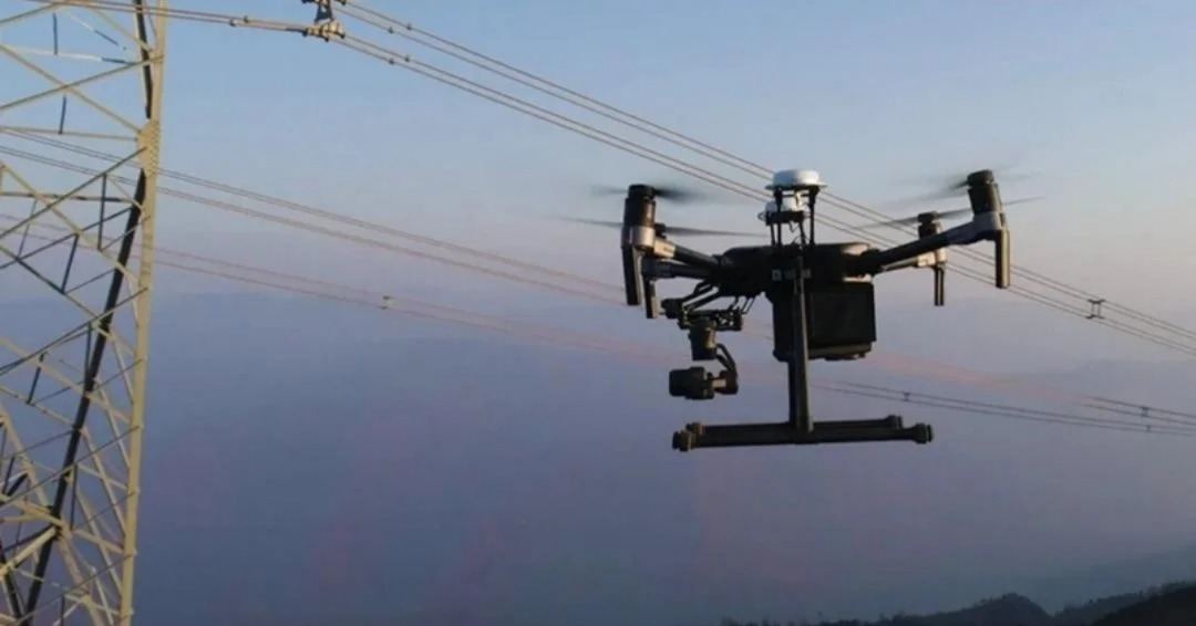 Drone inspecting power lines beside a transmission tower